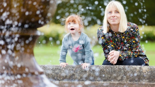 A lady smiling and a young girl with a face full of wonder watching water fall from a fountain at Powis Castle, Powys, Wales